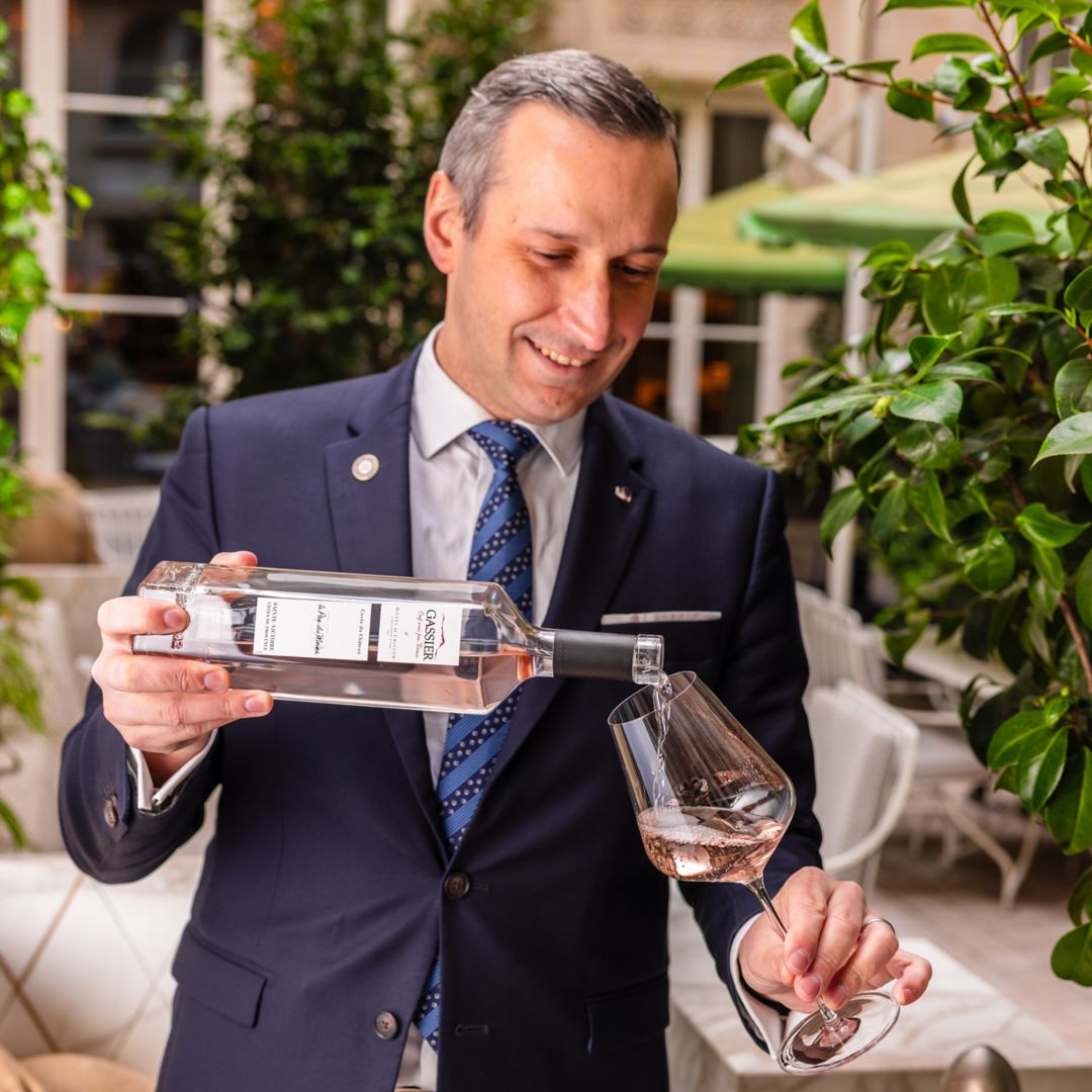 A man in a suit is pouring rosé wine from a bottle into a glass.